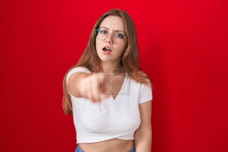 Foto de Joven mujer caucásica de pie sobre fondo rojo señalando disgustado y frustrado a la cámara, enojado y furioso con usted - Imagen libre de derechos