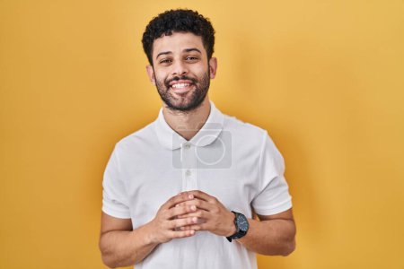 Photo for Arab man standing over yellow background hands together and fingers crossed smiling relaxed and cheerful. success and optimistic - Royalty Free Image