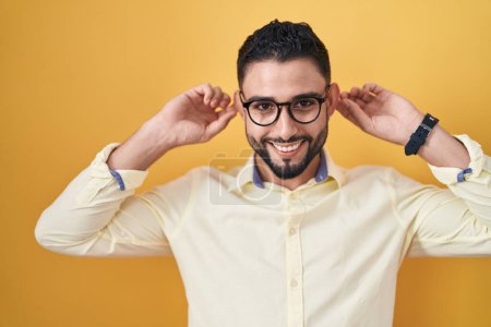 Photo for Hispanic young man wearing business clothes and glasses smiling pulling ears with fingers, funny gesture. audition problem - Royalty Free Image