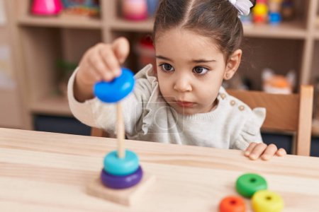 Téléchargez les photos : Adorable hispanique fille jouer avec cerceaux jouets assis sur la table à la maternelle - en image libre de droit