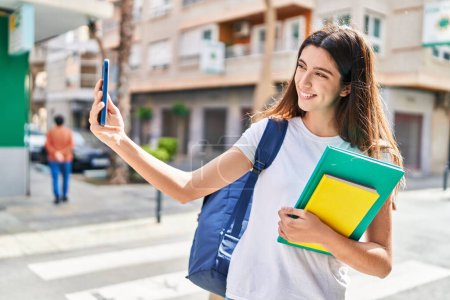 Foto de Joven mujer hispana hermosa estudiante sosteniendo libros hacen selfie por teléfono inteligente en la calle - Imagen libre de derechos