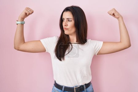 Photo for Young brunette woman standing over pink background showing arms muscles smiling proud. fitness concept. - Royalty Free Image