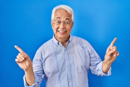 Foto de Hombre mayor hispano con gafas sonriendo confiado señalando con los dedos a diferentes direcciones. espacio de copia para publicidad - Imagen libre de derechos
