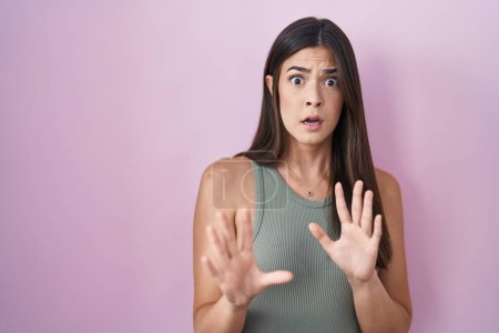 Photo for Hispanic woman standing over pink background afraid and terrified with fear expression stop gesture with hands, shouting in shock. panic concept. - Royalty Free Image