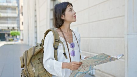 Téléchargez les photos : Jeune belle hispanique femme touristique souriant confiant tenant la carte de la ville à la rue - en image libre de droit