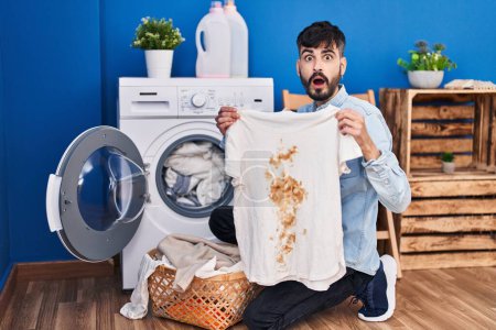 Photo for Young hispanic man with beard holding clean white t shirt and t shirt with dirty stain afraid and shocked with surprise and amazed expression, fear and excited face. - Royalty Free Image