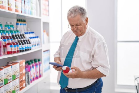 Photo for Middle age grey-haired man customer using smartphone holding medicine bottle at pharmacy - Royalty Free Image