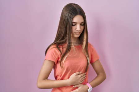 Photo for Teenager girl standing over pink background with hand on stomach because indigestion, painful illness feeling unwell. ache concept. - Royalty Free Image