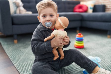 Photo for Adorable caucasian boy playing with baby doll sitting on floor at home - Royalty Free Image