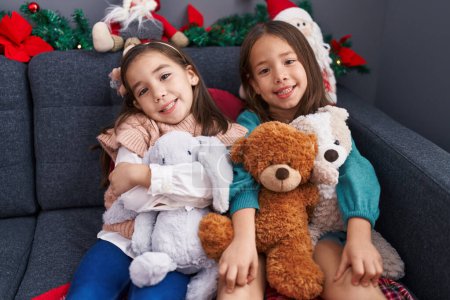 Photo for Adorable girls hugging teddy bear celebrating christmas at home - Royalty Free Image
