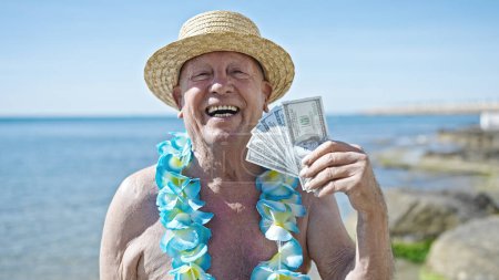 Photo for Senior grey-haired man tourist wearing swimsuit and summer hat holding dollars at seaside - Royalty Free Image