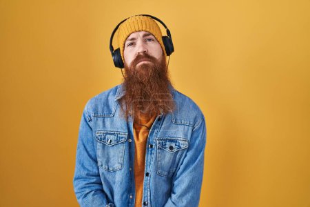 Téléchargez les photos : Homme caucasien à longue barbe écoutant de la musique à l'aide d'écouteurs à la recherche somnolent et fatigué, épuisé par la fatigue et la gueule de bois, les yeux paresseux le matin. - en image libre de droit