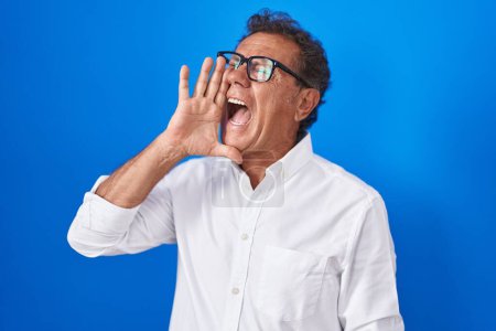 Photo for Middle age hispanic man standing over blue background shouting and screaming loud to side with hand on mouth. communication concept. - Royalty Free Image