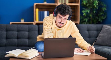 Photo for Young caucasian man using laptop and headphones studying at home - Royalty Free Image
