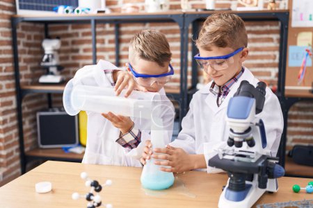 Foto de Adorable chicos estudiante vertiendo líquido en tubo de ensayo en el aula de laboratorio - Imagen libre de derechos