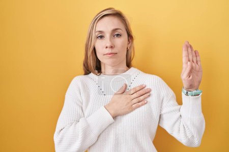 Photo for Young caucasian woman wearing white sweater over yellow background swearing with hand on chest and open palm, making a loyalty promise oath - Royalty Free Image