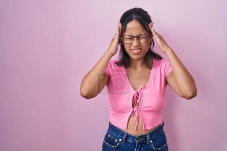 Foto de Mujer joven hispana de pie sobre fondo rosa con gafas con la mano en la cabeza para el dolor en la cabeza porque el estrés. padecer migraña. - Imagen libre de derechos