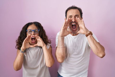 Téléchargez les photos : Couple hispanique du moyen âge ensemble sur fond rose criant à haute voix avec les mains sur la bouche - en image libre de droit