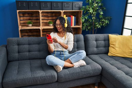 Foto de Mujer latina joven usando teléfono inteligente sentado en el sofá en casa - Imagen libre de derechos