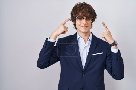 Téléchargez les photos : Entreprise hispanique jeune homme portant des lunettes souriant pointant vers la tête avec les deux doigts de la main, grande idée ou pensée, bonne mémoire - en image libre de droit