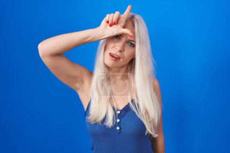 Téléchargez les photos : Femme caucasienne debout sur fond bleu se moquant des gens avec les doigts sur le front faisant geste perdant moquerie et insultant. - en image libre de droit