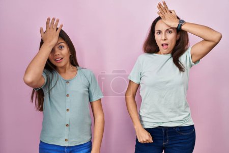 Photo for Young mother and daughter standing over pink background surprised with hand on head for mistake, remember error. forgot, bad memory concept. - Royalty Free Image