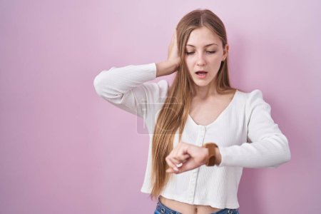 Téléchargez les photos : Jeune femme caucasienne debout sur fond rose regardant le temps de la montre inquiet, peur d'arriver en retard - en image libre de droit