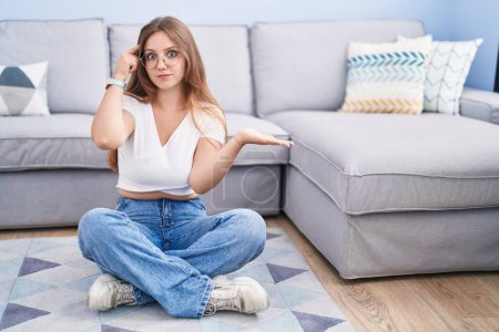 Photo for Young caucasian woman sitting on the floor at the living room confused and annoyed with open palm showing copy space and pointing finger to forehead. think about it. - Royalty Free Image