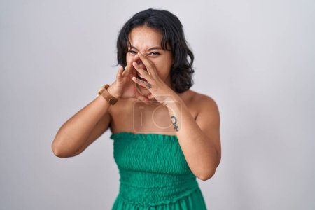 Foto de Mujer hispana joven de pie sobre un fondo aislado gritando furiosa en voz alta con las manos sobre la boca - Imagen libre de derechos