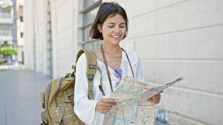 Foto de Joven hermosa mujer hispana turista sonriendo confiado sosteniendo mapa de la ciudad en la calle - Imagen libre de derechos