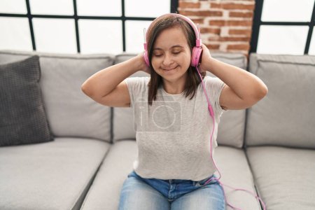 Foto de Síndrome de Down mujer escuchando música sentada en el sofá en casa - Imagen libre de derechos