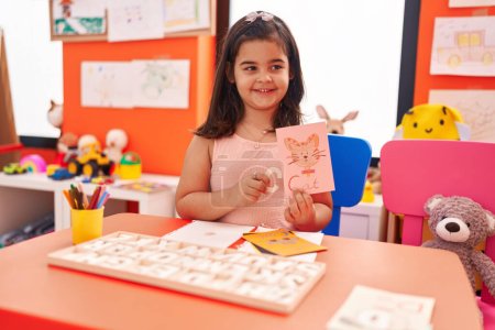 Téléchargez les photos : Adorable fille hispanique jouant avec le jeu de puzzle de vocabulaire assis sur la table à la maternelle - en image libre de droit