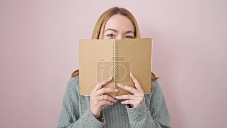 Photo for Young blonde woman covering face with book over isolated pink background - Royalty Free Image