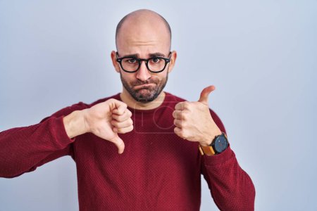 Photo for Young bald man with beard standing over white background wearing glasses doing thumbs up and down, disagreement and agreement expression. crazy conflict - Royalty Free Image