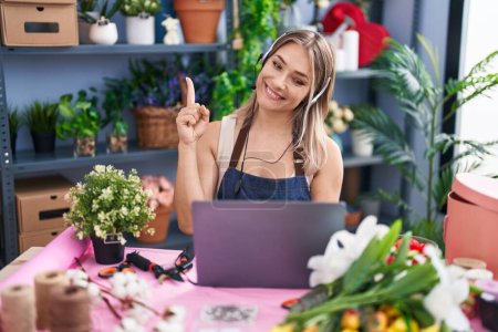 Foto de Mujer rubia caucásica que trabaja en floristería en línea sonriendo con una idea o pregunta apuntando con el dedo con la cara feliz, número uno - Imagen libre de derechos