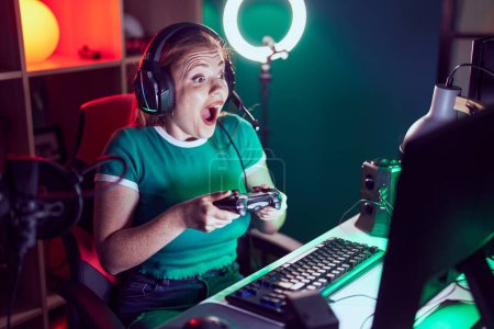 Photo for Young redhead woman streamer playing video game using joystick at gaming room - Royalty Free Image