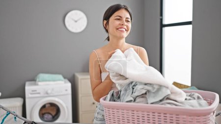 Photo for Young beautiful hispanic woman smiling confident smelling clean clothes at laundry room - Royalty Free Image