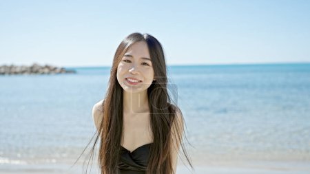 Téléchargez les photos : Jeune femme chinoise touriste souriant en maillot de bain confiant au bord de la mer - en image libre de droit