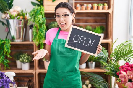 Photo for Hispanic young woman working at florist holding open sign celebrating achievement with happy smile and winner expression with raised hand - Royalty Free Image