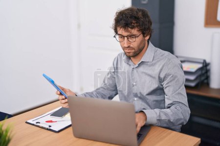Foto de Joven trabajador de negocios hispano usando touchpad y laptop en la oficina - Imagen libre de derechos