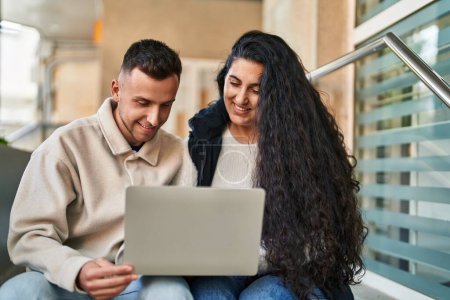 Téléchargez les photos : Homme et femme souriant confiant en utilisant un ordinateur portable à la rue - en image libre de droit