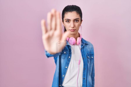 Photo for Young beautiful woman standing over pink background doing stop sing with palm of the hand. warning expression with negative and serious gesture on the face. - Royalty Free Image