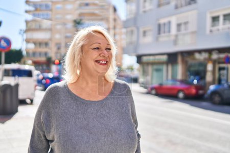Foto de Mujer rubia de mediana edad sonriendo confiada de pie en la calle - Imagen libre de derechos