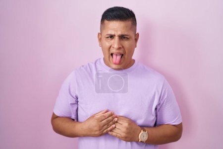 Foto de Joven hombre hispano de pie sobre fondo rosa sacando la lengua feliz con expresión divertida. concepto de emoción. - Imagen libre de derechos