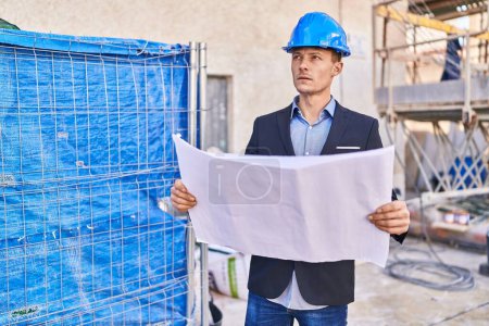 Photo for Young man architect standing with relaxed expression looking blueprint at street - Royalty Free Image