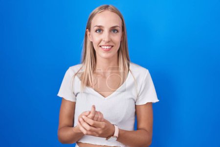 Photo for Young caucasian woman standing over blue background with hands together and crossed fingers smiling relaxed and cheerful. success and optimistic - Royalty Free Image