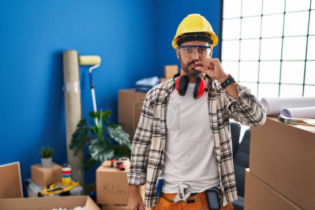 Téléchargez les photos : Jeune homme hispanique avec barbe travaillant à la maison rénovation bouche et lèvres fermées comme zip avec les doigts. secret et silencieux, tabou parlant - en image libre de droit