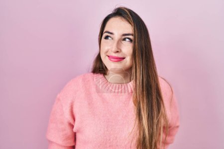 Foto de Young hispanic woman standing over pink background smiling looking to the side and staring away thinking. - Imagen libre de derechos