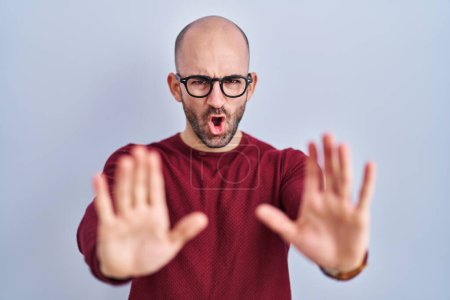 Photo for Young bald man with beard standing over white background wearing glasses doing stop gesture with hands palms, angry and frustration expression - Royalty Free Image