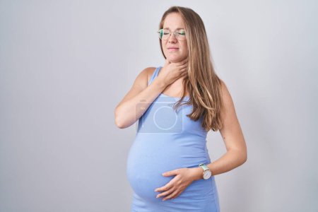 Téléchargez les photos : Jeune femme enceinte debout sur fond blanc touchant le cou douloureux, mal de gorge pour la grippe, la motte et l'infection - en image libre de droit